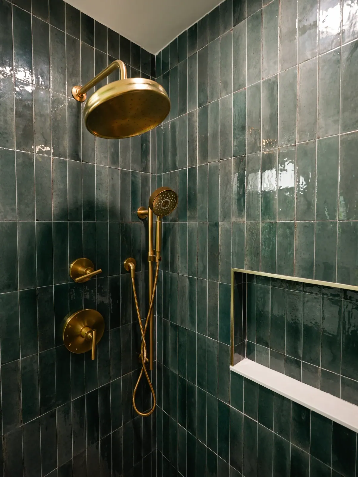Green tile shower with brushed brass fixtures and a niche