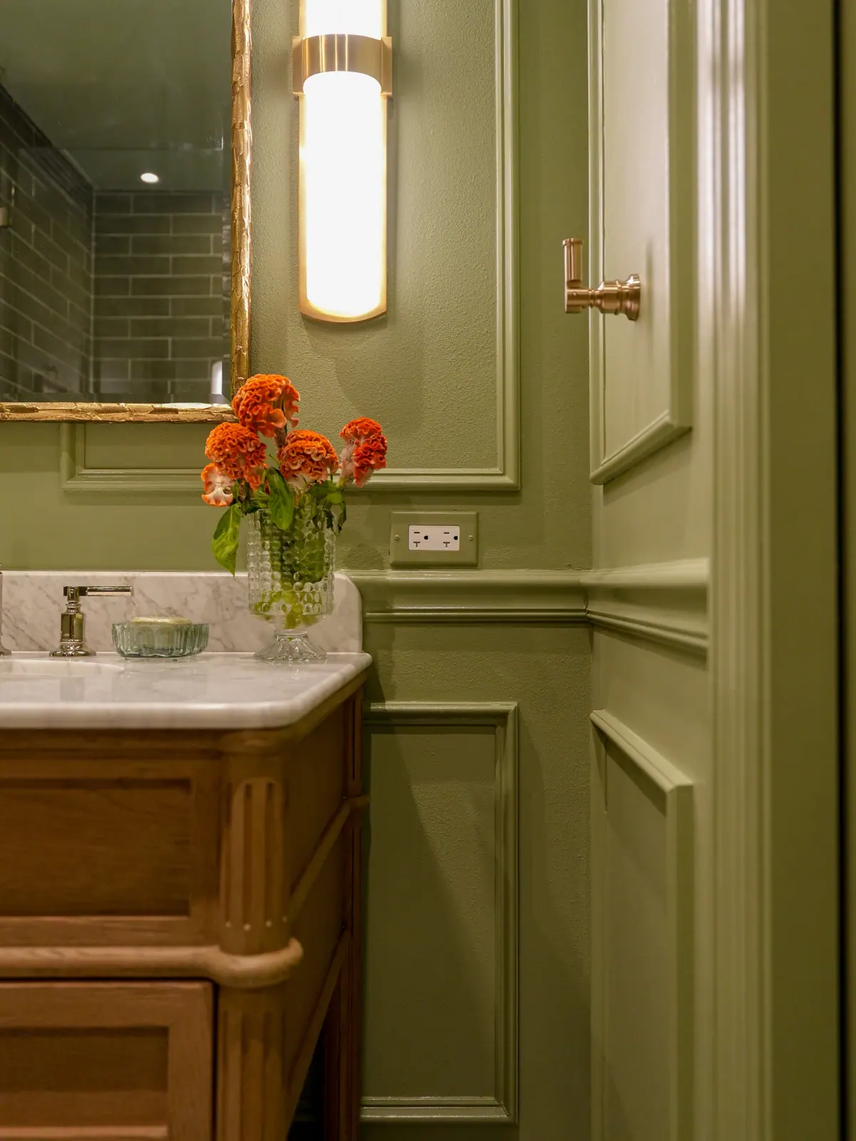 Olive paneled walls with a wood vanity and flowers