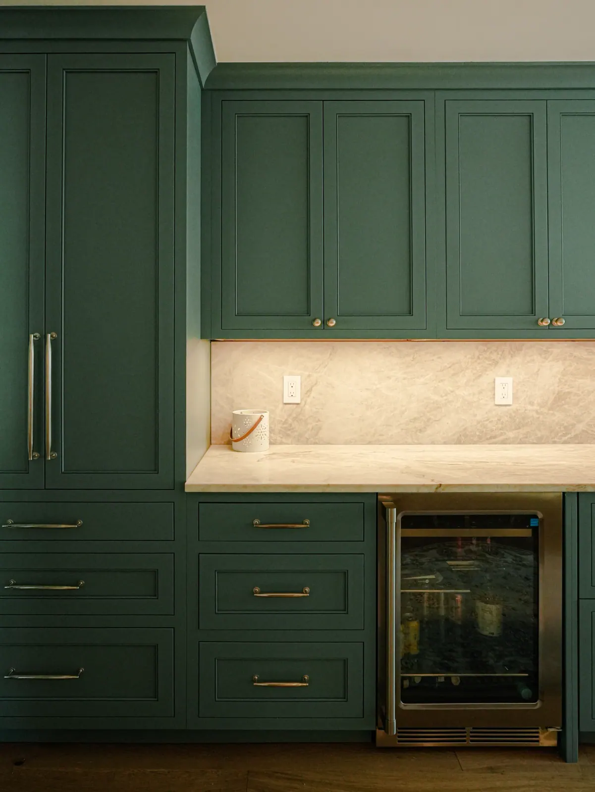 Deep green shaker cabinetry with a stone backsplash and brass pulls